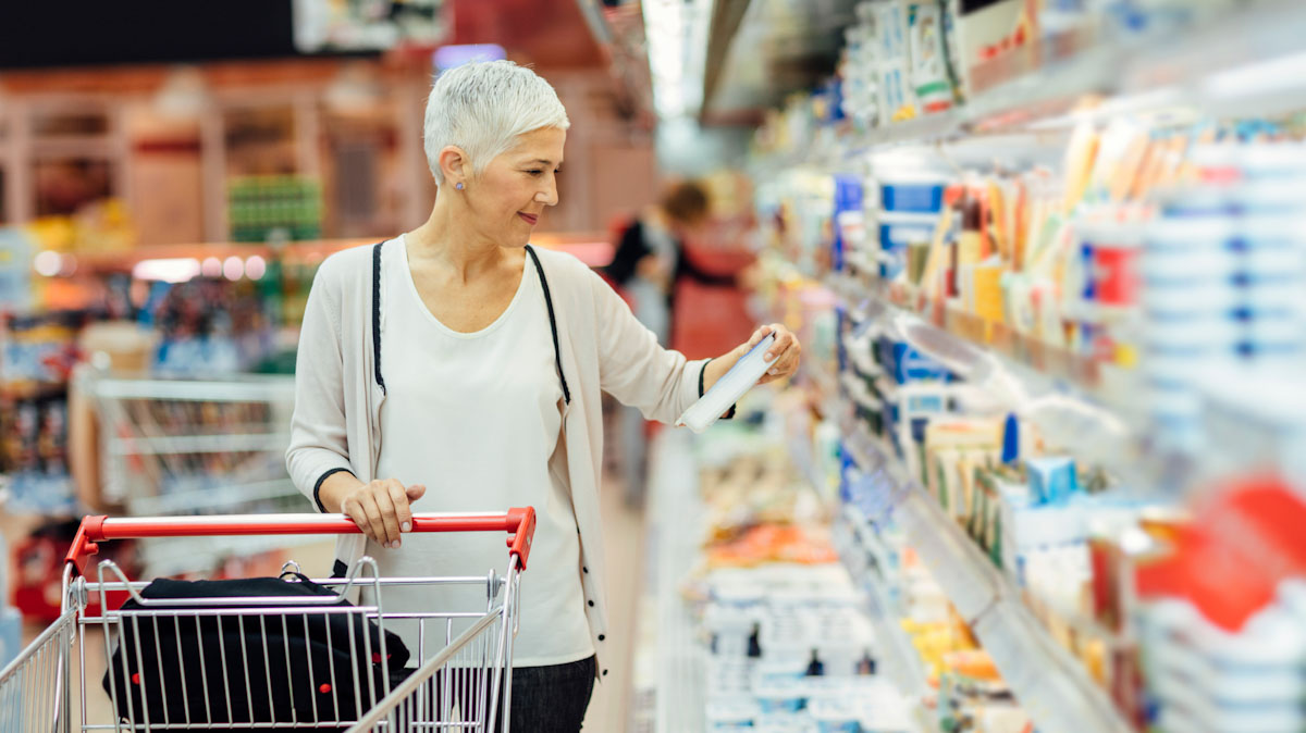 A mature woman shops for groceries and inspects a nutrition fact panel.