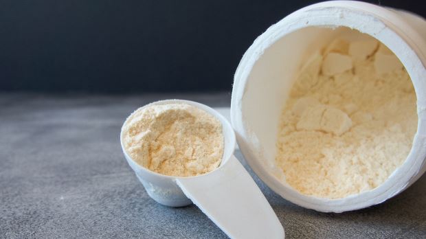 A container of bovine colostrum powdered supplement laying on its side, with a scoop of supplemental powder next to it.