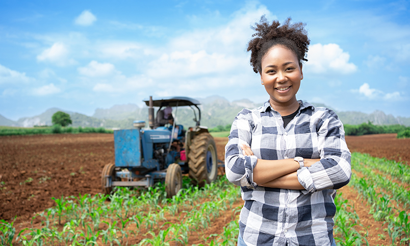 Woman farmer in field on a farm with a tractor inspecting crops.