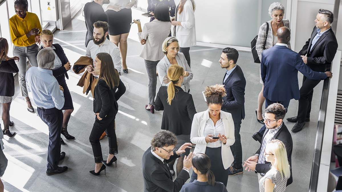 A diverse group of male and female business professionals actively networking at a conference. Attendees in formal attire discuss ideas and opportunities in a modern venue, highlighting collaboration and innovation in the corporate world.