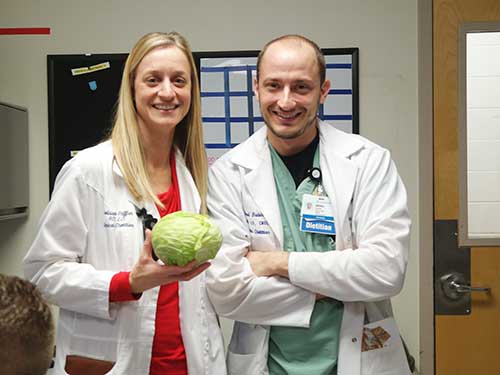 An image of a dietetic intern and preceptor standing next to each other and the intern holding a head of lettuce.