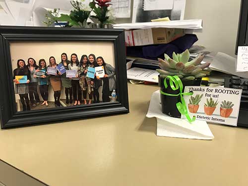 An image of a group of dietetic interns in a picture frame on a desk next to a small gift.