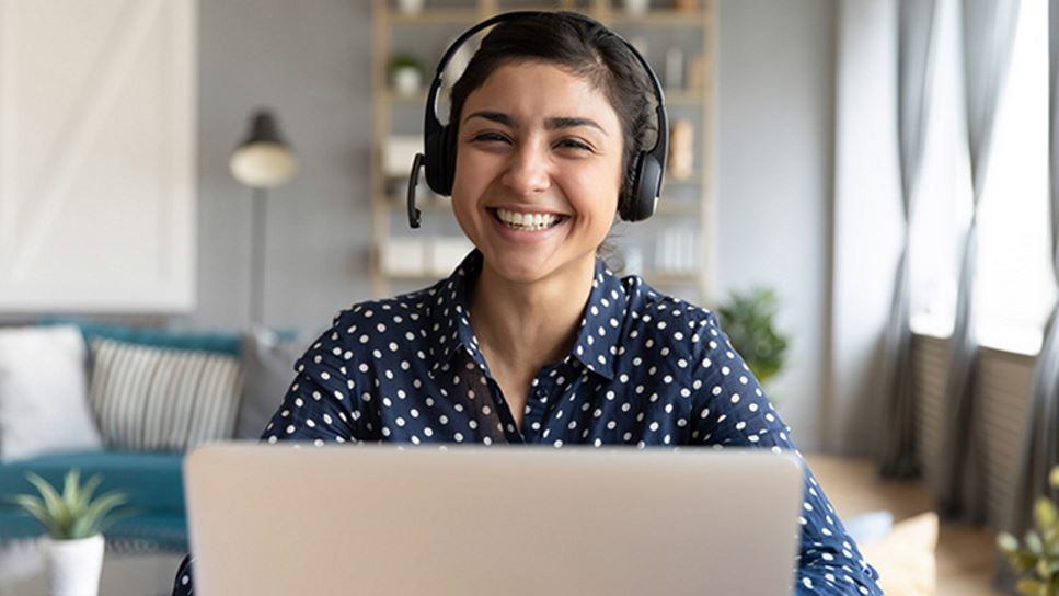 woman smiling and wearing headphones in front of a laptop