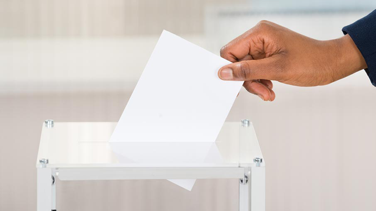 close-up of hand dropping ballot in slot on voting box