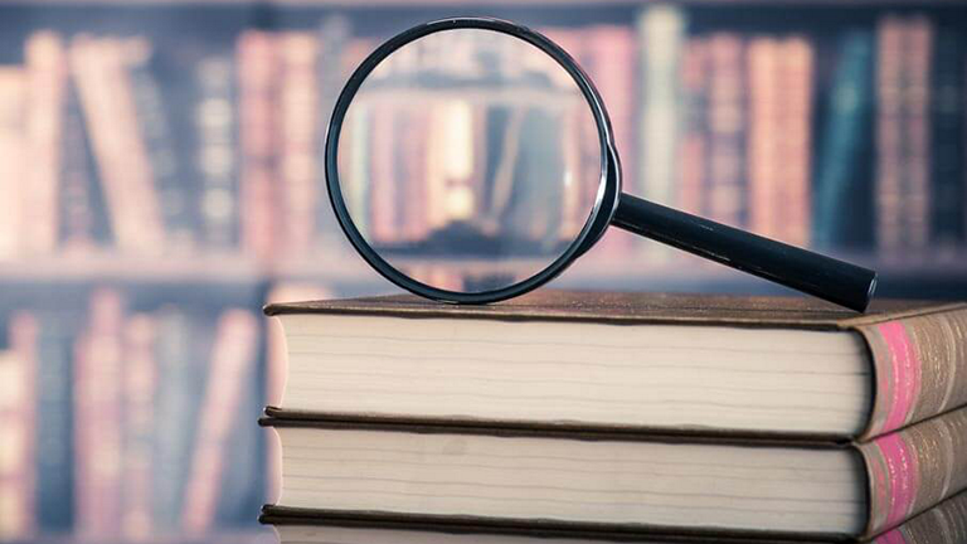 magnifying glass on stack of textbooks