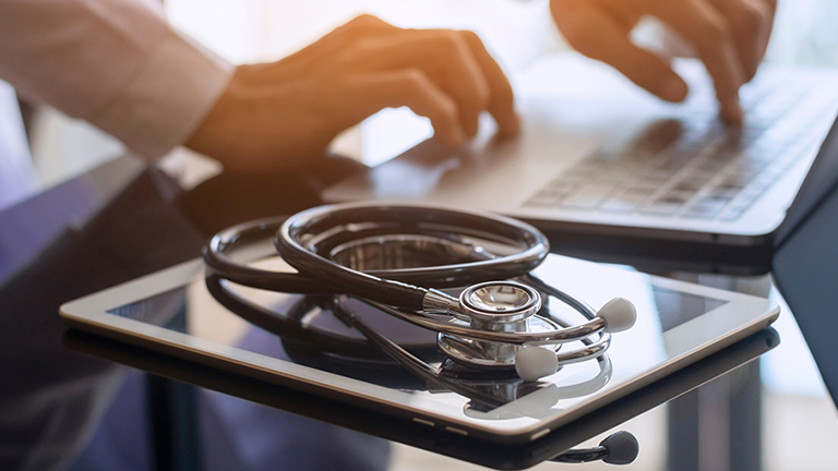 hands typing on a laptop with mobile tablet next to computer