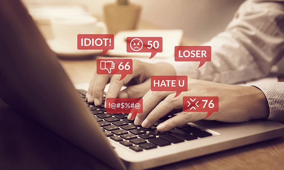 Typing on laptop with thought bubbles saying mean things like "idiot" and "loser"