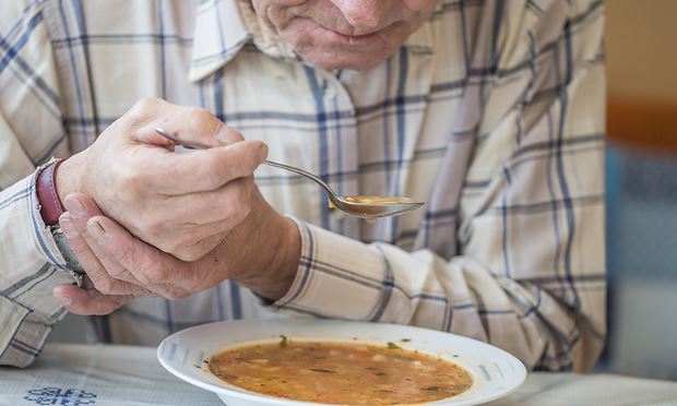 Man with Parkinson's disease eating soup while holding hand steady.