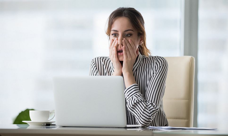 woman expressing horror and regret while sitting in front of laptop