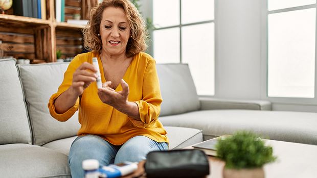 A woman with type 2 diabetes is measuring her glucose sitting on the sofa at home.