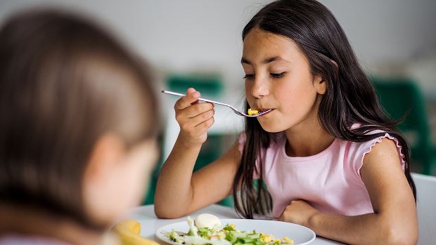 Child in lunch room eating healthy meal.