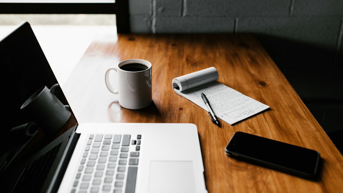 Desk with a laptop, notepad and pen, coffee, and cellphone
